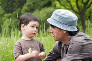 Father with toddler son talking on a green summer meadow.